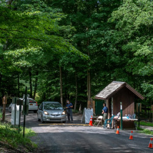 A car stops at the trailhead booth at Spring Farm, a Trailhead Assistant stands next to the car
