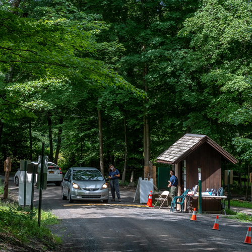 Spring Farm Trailhead Visitor Contact booth to the right, with a Trailhead Assistant standing outside. A car is in the center with another Trailhead Assistant standing near the window