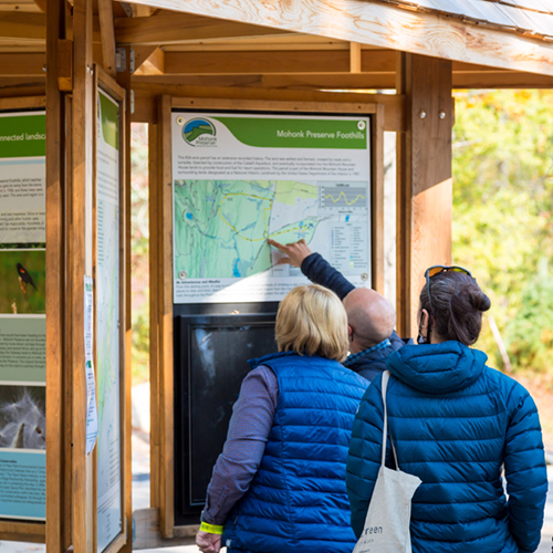 Three visitors look at an information kiosk, one points to a map