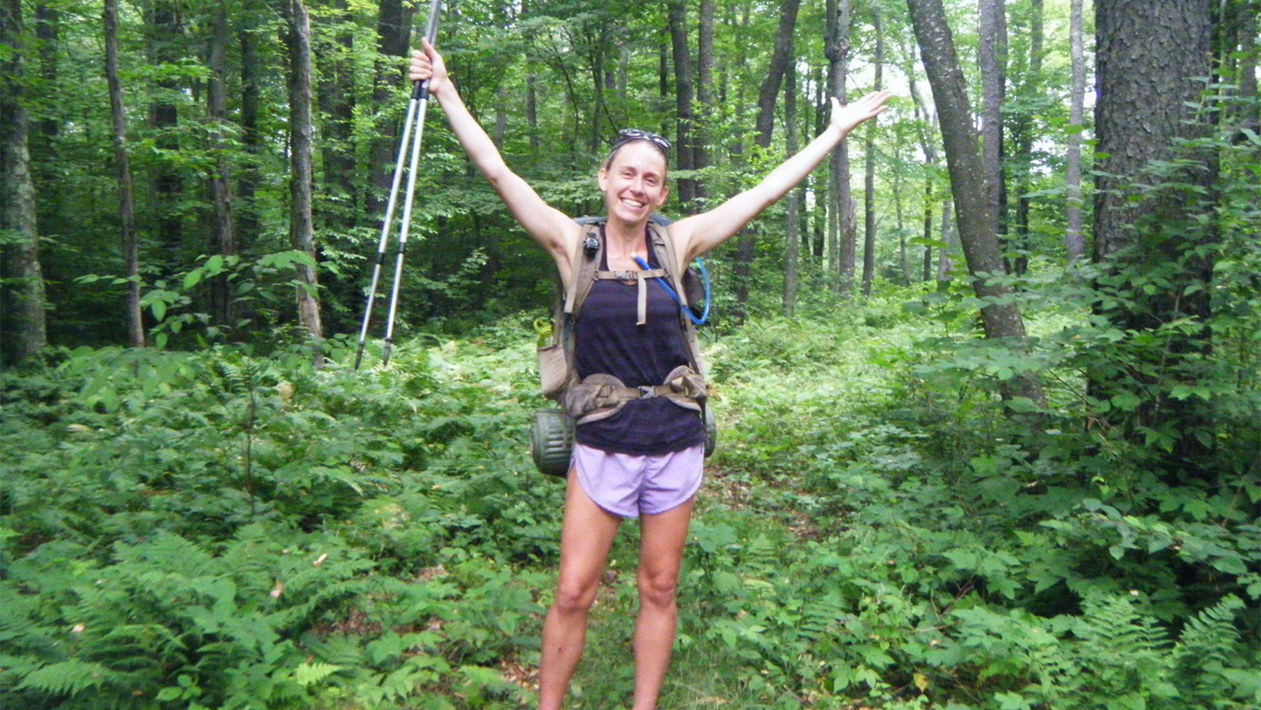 Heather Houskeeper with her arms in the air with a forest in the background