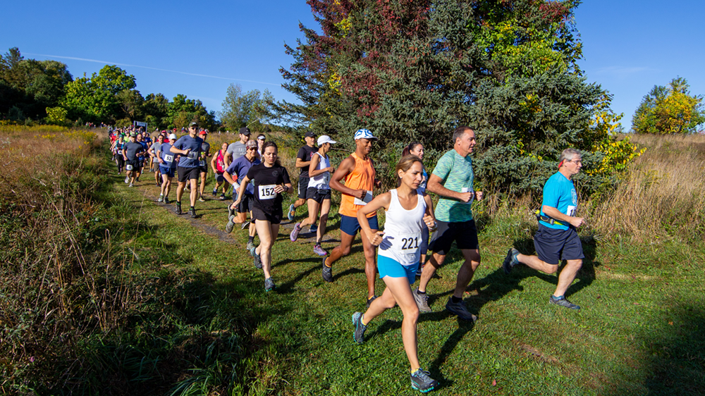 Runners moving toward the camera on a mowed path, with the race start line in the background.
