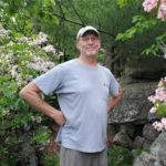 Volunteer standing in front of Mountain Laurel on a trail