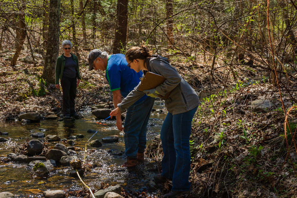 Three people look at a running stream of water to collect research