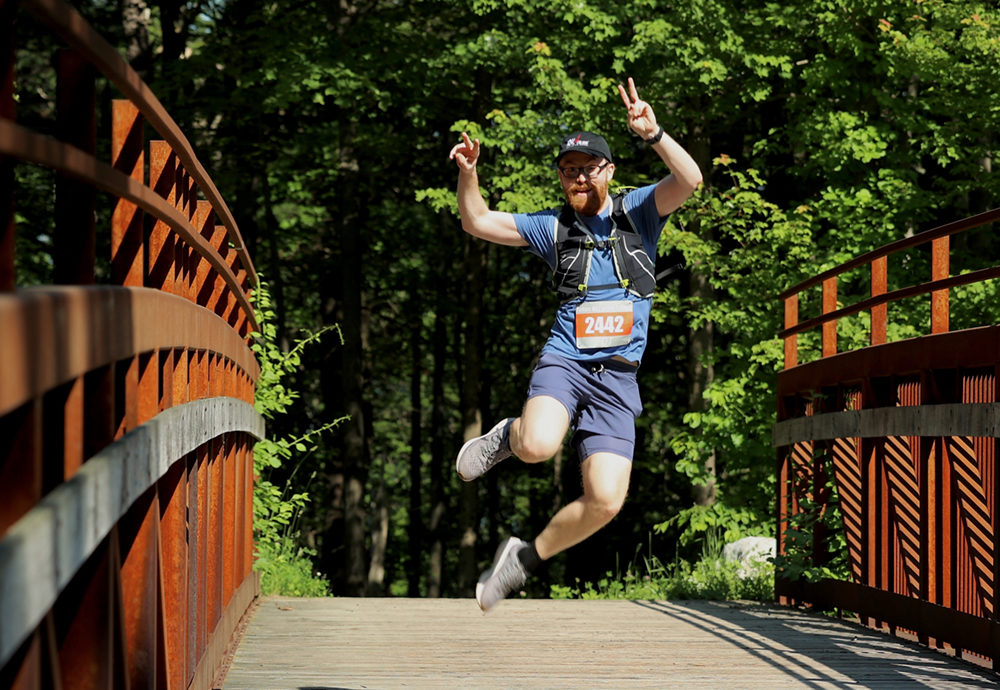 Runner in the Annual Rock and Snow Bridge 2 Bridge race jumps in the air mid run on the cedar road bridge