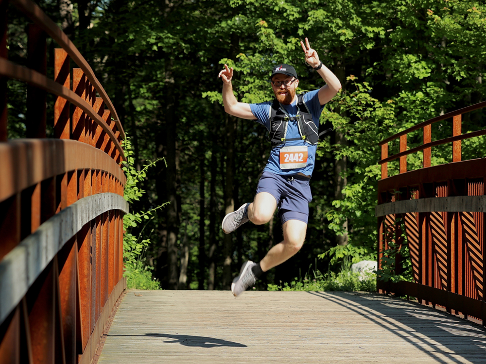 Runner in the Annual Rock and Snow Bridge 2 Bridge race jumps in the air mid run on the cedar road bridge