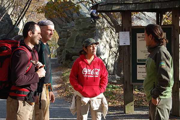 Group of climbers attend a public program led by Mohonk Preserve Ranger Frank Tkac on Undercliff Carriage Road. Exposed rock and informative kiosk in the background.
