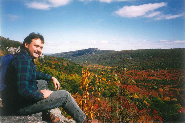Man sitting on cliff overlooking a vista or rolling mountains in fall
