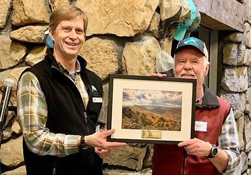Two men pose with a framed photo of the Shawangunk Mountains in the Mohonk Preserve Visitor Center