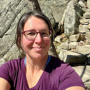 Heidi McCowan smiles on a sunny day outside near a rock wall